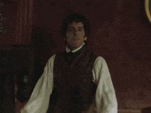a man wearing a vest and a white shirt is standing in front of a red wall