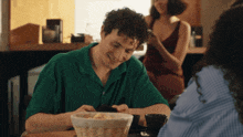 a man in a green shirt sits at a table with a basket of bread on it