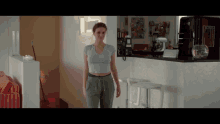 a woman in a crop top and sweatpants is walking in a kitchen