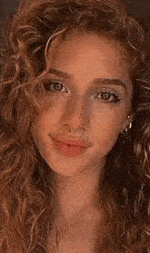 a close up of a woman 's face with curly hair , earrings , and a nose ring .