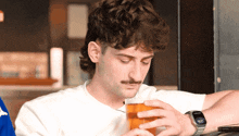 a man with a mustache is drinking a glass of beer while looking at his watch