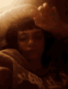 a woman is laying in bed with her eyes closed and her hand on her head .