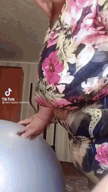 a woman in a floral dress is playing with a blue exercise ball .