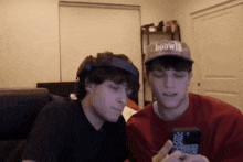 two young men wearing virtual reality headsets are looking at a cell phone .