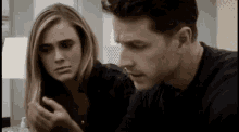 a man and a woman are sitting next to each other looking at a cell phone .