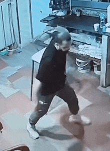 a man in a black shirt and gray pants is standing in a kitchen .
