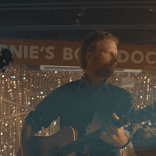 a man playing a guitar in front of a sign that says " e 's ndock "
