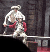 a man in a red jacket is sitting on a bench while another man jumps over him