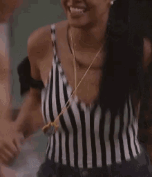 a woman wearing a black and white striped tank top is smiling and holding a whistle .