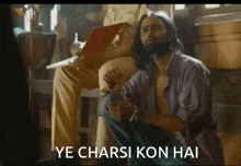 a man with long hair and a beard is squatting down with the words ye charsi kon hai written below him