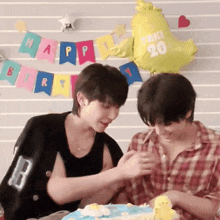 two men are sitting at a table with a cake and balloons .