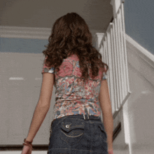 a woman wearing a floral shirt and denim skirt is walking down stairs