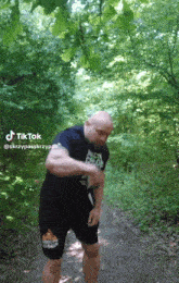 a man in a black shirt and black shorts is standing on a path in the woods