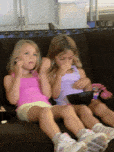 two young girls sitting on a couch eating popcorn