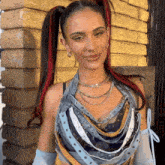 a woman with pigtails and a necklace that says ' i love you ' on it stands in front of a brick wall