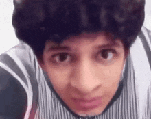 a young man with curly hair and a striped shirt is looking at the camera .