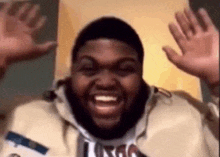 a man with a beard is laughing and raising his hands in the air .