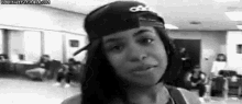 a black and white photo of a woman wearing a baseball cap and making a funny face .