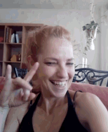 a woman in a black tank top is smiling and giving the peace sign