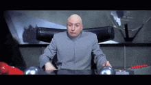 a bald man in a gray suit is sitting at a desk with two balls on it .