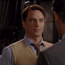 a man wearing a yellow vest and tie is talking to another man
