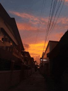 a sunset over an alleyway with a few buildings and telephone wires