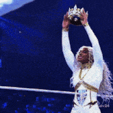 a woman in a white outfit is holding a crown over her head in a wrestling ring