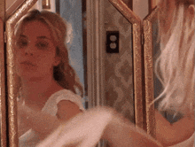 a woman is looking at herself in a mirror with a light switch on the wall