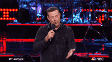 a man holding a microphone on a stage with a nbc logo behind him
