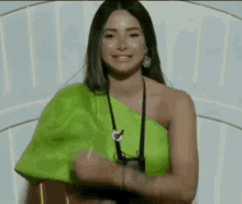 a woman in a neon green one shoulder top is standing in front of a white wall and smiling .