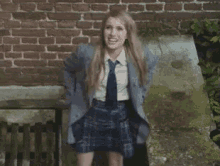 a girl in a school uniform is giving the middle finger in front of a brick wall .