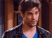 a man wearing a black leather jacket and a blue shirt is standing in a room .