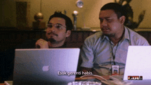 two men are sitting at a table looking at a laptop and one of them says " esok gerenti habis "