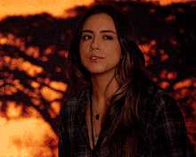 a woman wearing a plaid shirt and a necklace is looking at the camera