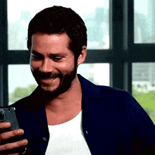a man with a beard is laughing while looking at his phone