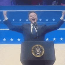 a man in a suit and tie is standing at a podium with his hands in the air