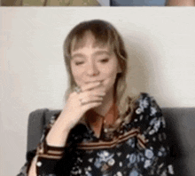 a woman is sitting on a couch with her hand over her mouth .