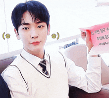 a young man in a white shirt and tie is holding a pink piece of paper with chinese writing on it