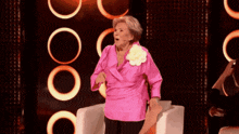 a woman in a pink shirt with a flower on her shoulder is dancing on a stage