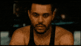 a man with a beard and a black tank top looks at the camera