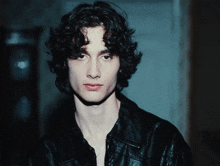 a young man with curly hair is wearing a black jacket