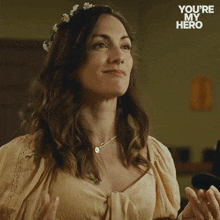 a woman with a flower crown on her head is clapping with the words you 're my hero behind her