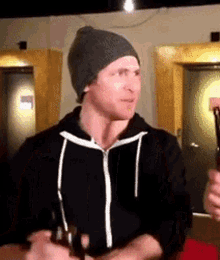 a man wearing a beanie and a black jacket is holding a beer bottle .
