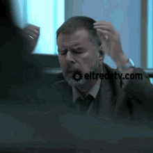 a man with a beard is sitting at a desk in front of a screen that says eltrecetv.com .