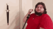 a man in a red shirt holds a sword in front of a sword hanging on the wall