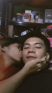 a woman kissing a man 's cheek in front of a shelf with a jar of nescafe on it