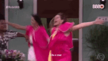 a group of women in pink dresses are dancing in front of a door with their arms in the air .