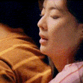 a close up of a woman 's face with her eyes closed and a pink shirt on .