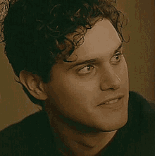 a close up of a young man 's face with curly hair and a black shirt .