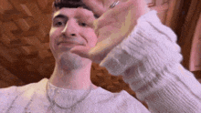 a man wearing a white sweater and a necklace is making a funny face with his hand .